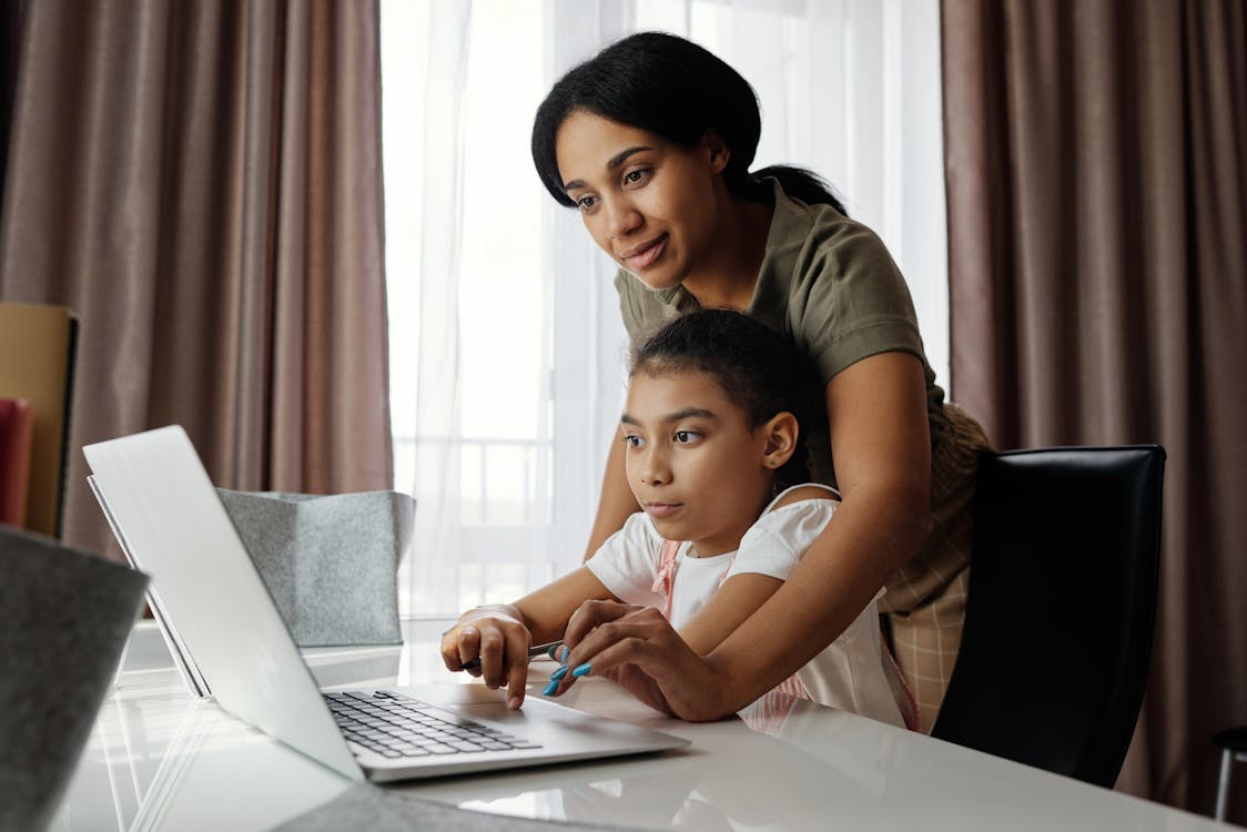 Mother helping her daughter use a laptop at home