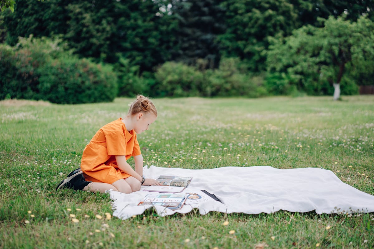 Child reading a book on a blanket outdoors in summer
